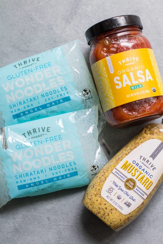Thrive market salsa, mustard and wonder noodles on a grey background.